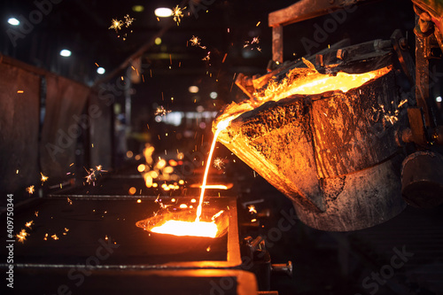 Molten metal casting in foundry. Filling mold with hot liquid iron and producing iron components in steel plant. photo