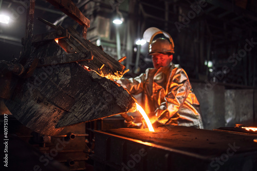 Foundry hardworking people pouring hot liquid iron from bucket into molds. Iron ore production and metallurgy. photo