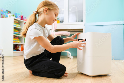 Primary school age blonde girl enjoy comfort at home with air humidifier white box  health care and modern devices