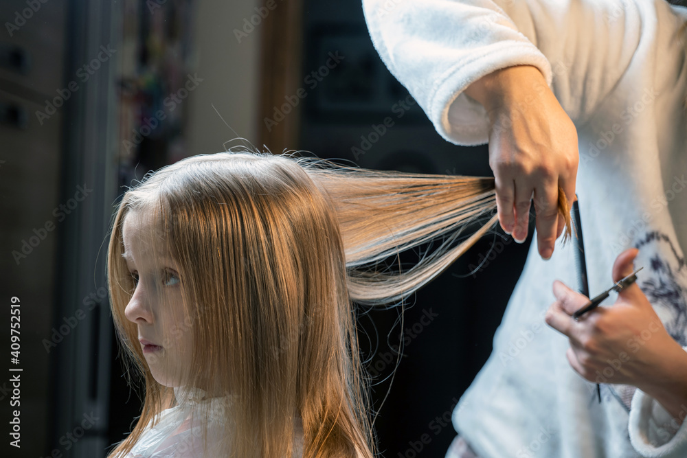 Fototapeta premium hair cutting at home, mom cuts daughter's hair in the kitchen