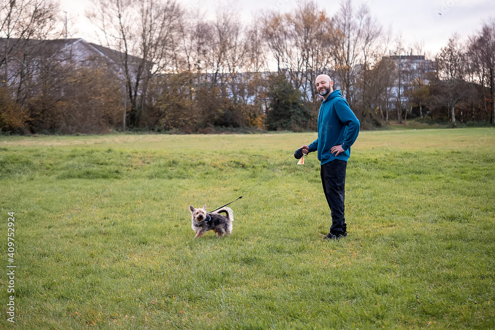Bald man in blue jacket with his Yorkshire pet terrier in a park. Pet care and friendship concept Bald man in blue jacket with his Yorkshire pet terrier in a park. Pet care and friendship concept