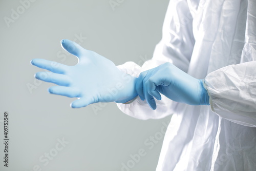 Doctor in a protective suit puts on blue rubber gloves