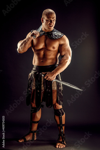 Severe barbarian in leather costume with two swords. Portrait of balded muscular gladiator. Studio shot. Black background.