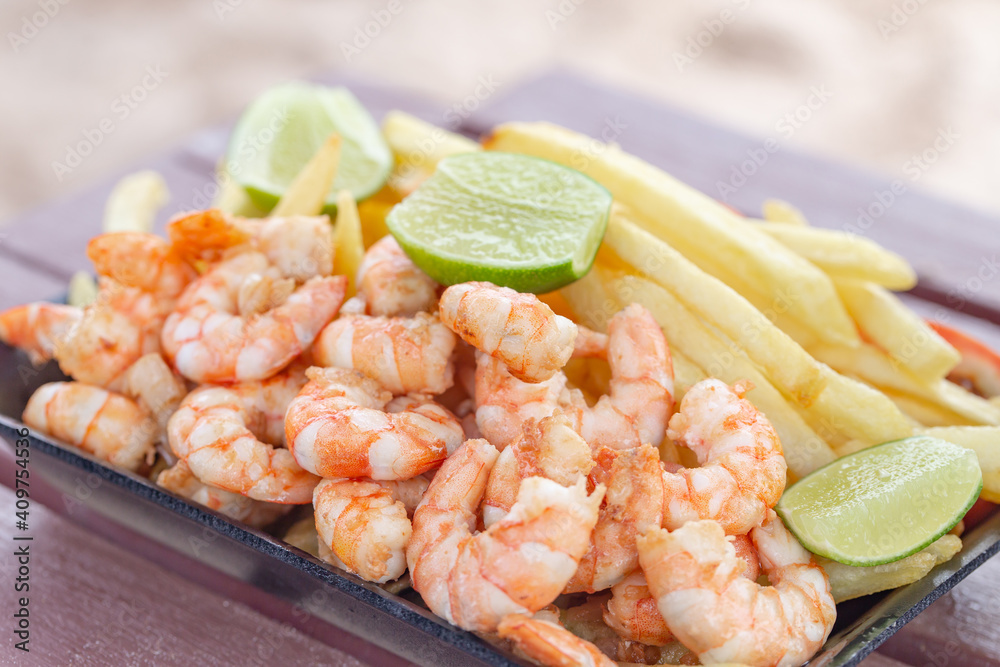 Shrimp snack accompanied by potato. Traditional taste of beaches in northeastern Brazil. Juicy shrimp served with fries and green lemon on the beach. 