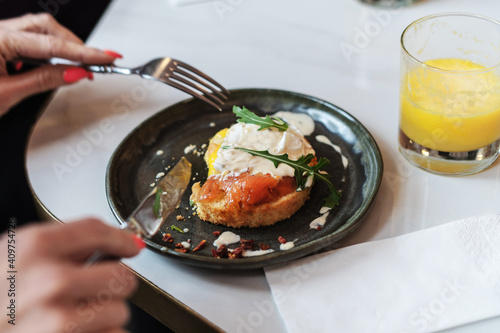 Woman hands holding fork and knife and having breakfast. Smoked salmon sandwich with cream cheese on plate close-up, glass of orange juice, napkin. Selective Focus