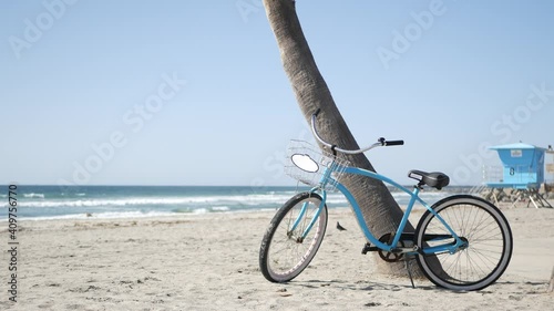 Blue bicycle, cruiser bike by ocean beach, pacific coast, Oceanside California USA. Summertime vacations, sea shore. Vintage cycle on sand near lifeguard tower or watchtower hut. Sky and water waves.