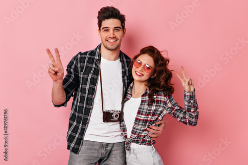Couple in love posing in checkered shirts. Studio shot of brunette man embracing girlfriend on pink background.