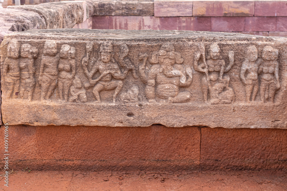 Aihole, Karnataka, India - November 7, 2013: Huchchimalli Gudi or Temple. Closeup of small brown stone fresco featuring Ganesha at center on red stone wall of tank.