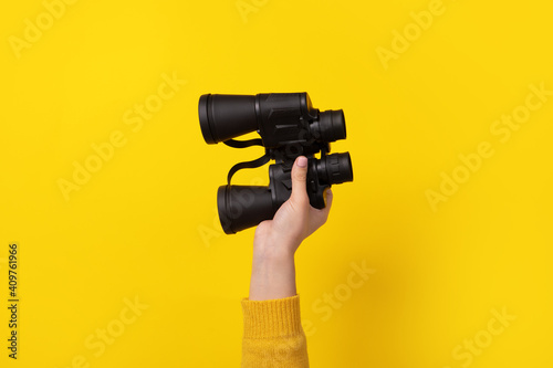 binoculars in hand over yellow background, search concept.