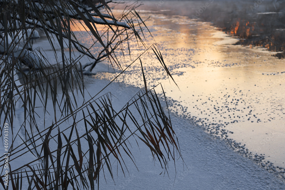 River winter landscape. Frost on ice. Fog over a non-freezing river at sunset. River winter landscape. Frost on ice. Fog over a non-freezing river at sunset.