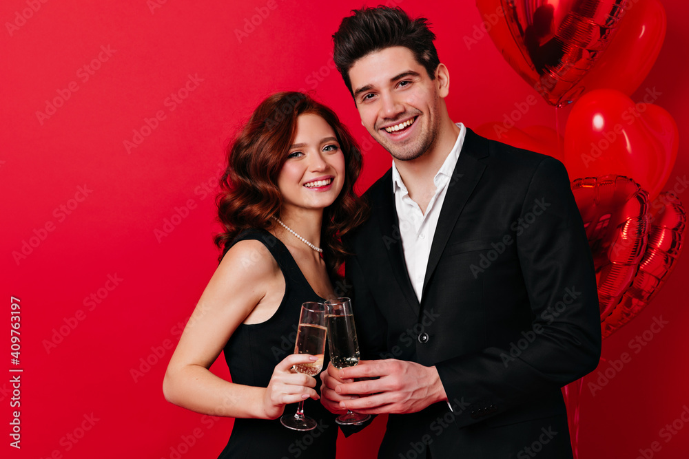 Studio shot of married couple isolated on red. Laughing young people posing with wineglasses at party. Studio shot of married couple isolated on red. Laughing young people posing with wineglasses at party.