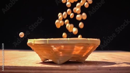 Soybeans falling into a bamboo basket on wooden table in slow motion. Freshly harvested soy fall into bammboo basket on black background. photo