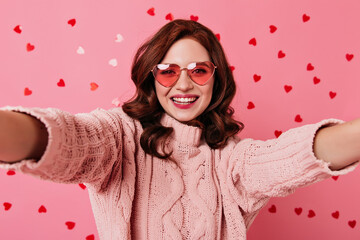 Pretty ginger girl smiling on pink background. Studio shot of caucasian lady making selfie in valentine's day.
