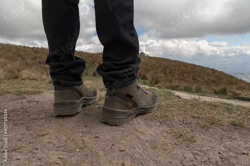 detail of a man's feet with boots and jeans on a hill with dirt and a background of the sky with clouds