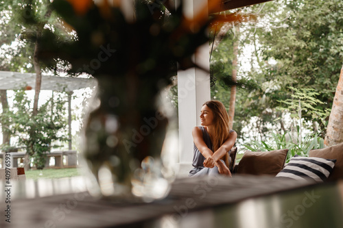 Home lifestyle woman relaxing enjoying luxury sofa patio furniture on outdoor patio living room. Young woman sitting on chair in green garden terrace