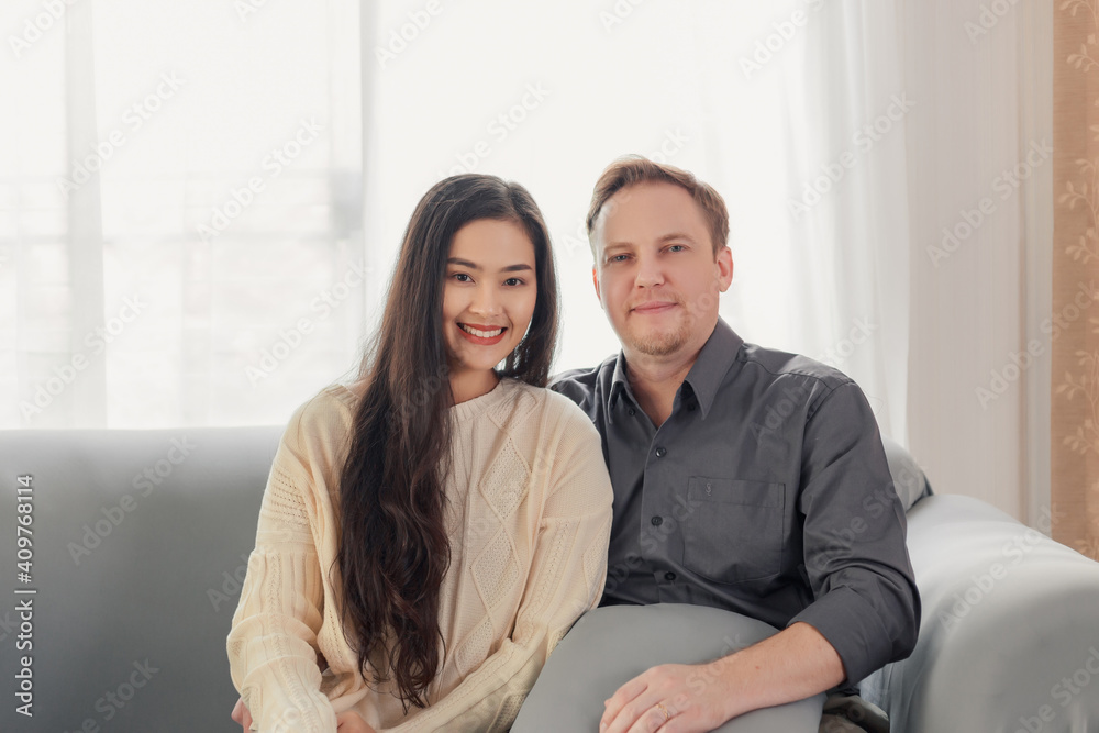 Young happy married interracial couple with smiley face sitting on couch at home Young happy married interracial couple with smiley face sitting on couch at home