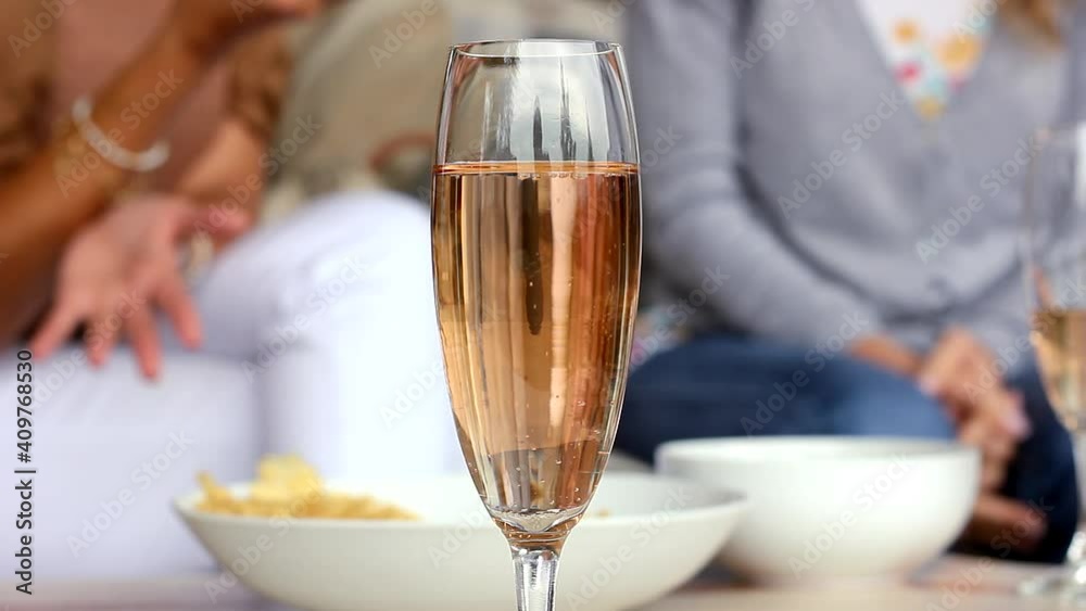 Sparkling rose wine glass and women eating snacks on background. Friends meeting, party celebration concepts