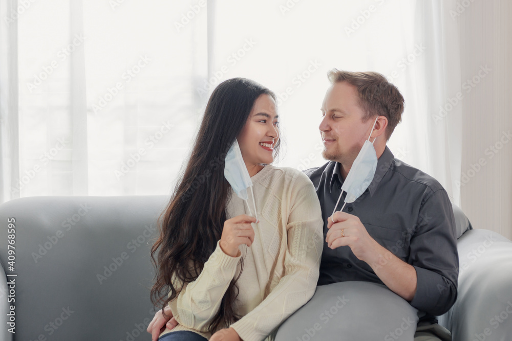 Young married interracial couple taking the face mask off after pandemic crisis finish with smiley face at home Young married interracial couple taking the face mask off after pandemic crisis finish with smiley face at home