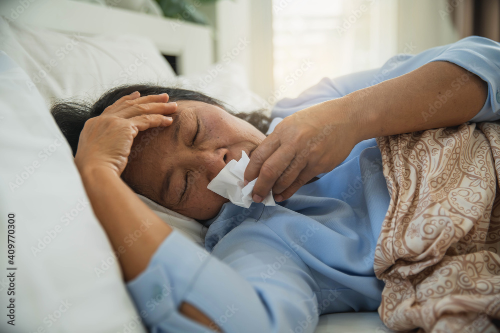 Old woman feels so sick. Sick middle aged woman sneezing blowing running nose holding tissue sit on bed. coronavirus CoVid-19. people and virus concept Old woman feels so sick. Sick middle aged woman sneezing blowing running nose holding tissue sit on bed. coronavirus CoVid-19. people and virus concept