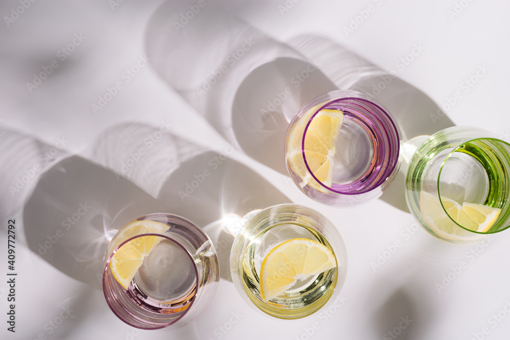 Colorful glasses with refreshing of water with slice of citrus inside on white background. Summer creative flat lay with hard shadows. Colorful glasses with refreshing of water with slice of citrus inside on white background. Summer creative flat lay with hard shadows.