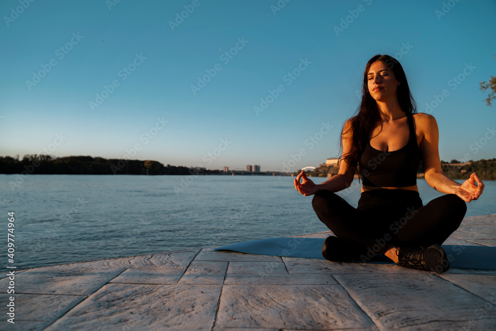 Beautiful young woman relaxing by the river in sunset and meditating, soaking in the sun 