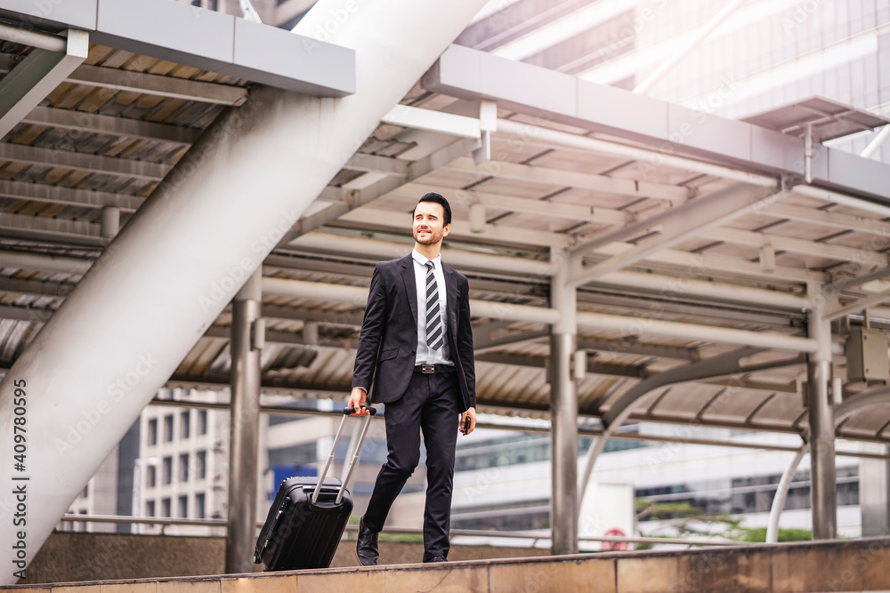Caucasian businessman confidently walking through the urban city district while holding and dragging along his black suit case, wearing formally black suit and tie with city skylines at the background Caucasian businessman confidently walking through the urban city district while holding and dragging along his black suit case, wearing formally black suit and tie with city skylines at the background