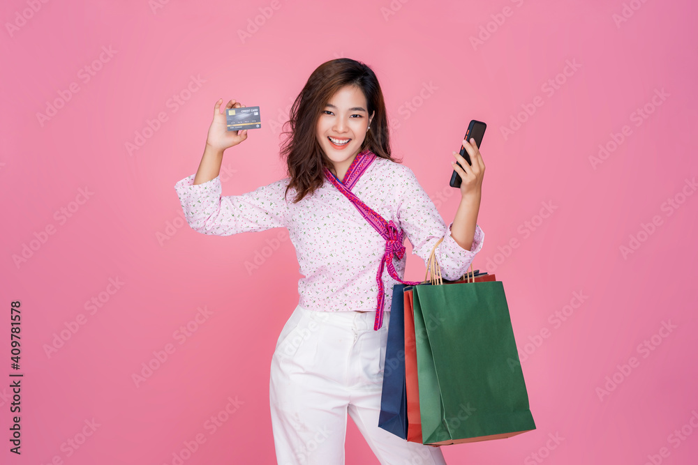 Asian woman online shopping bag sales using credit card mobile phone technology purchasing products online transaction payment happy smiling beautiful attractive, model studio pink isolated background Asian woman online shopping bag sales using credit card mobile phone technology purchasing products online transaction payment happy smiling beautiful attractive, model studio pink isolated background