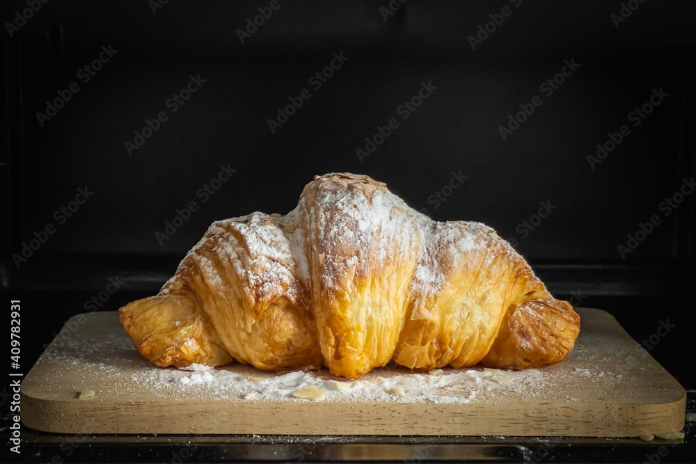 Croissant on a wooden plate with icing sugar and almonds on a black background. Select focus