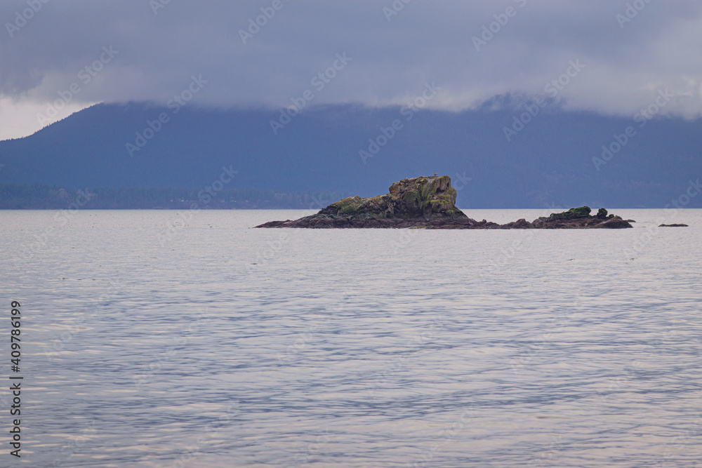 Rocky sandstone outcroppings in an ocean bay with a misty island in the distance partially hidden by low cloud