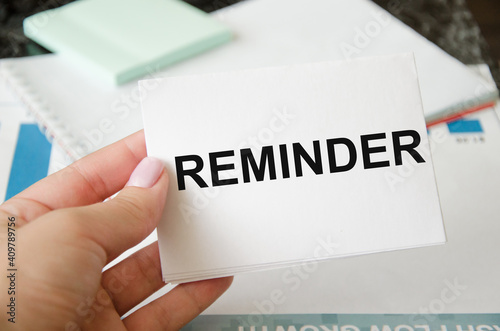 word reminder written on a white sheet of paper which is held by a man on the background of a financial chart