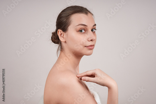 Portrait of a lovely young woman in profile with bare shoulders, touching her shoulder, looking at the camera Isolate on a gray background.