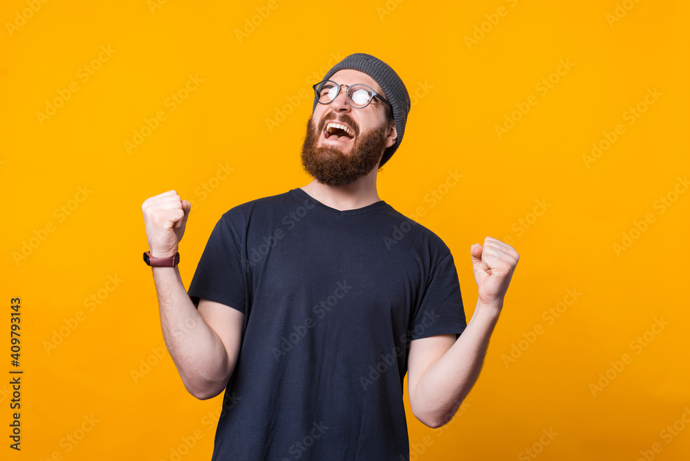 A young hipster with beard is screaming of happiness holding his both hands up .