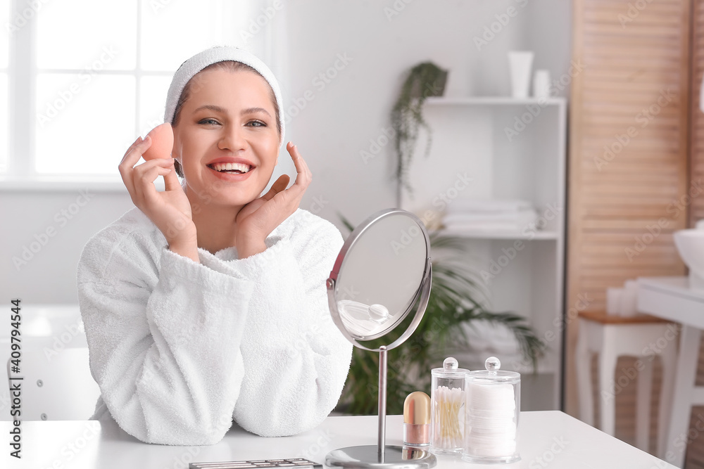 Beautiful young woman with sponge applying makeup at home Beautiful young woman with sponge applying makeup at home