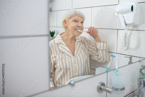 Elderly woman brushing her teeth in the bathroom