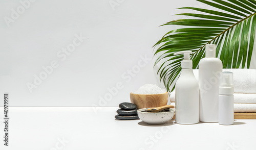 White cosmetic bottles with spa element and towel with palm leaf on white background. Blank label for branding mock-up. Natural beauty product concept. Copy space.