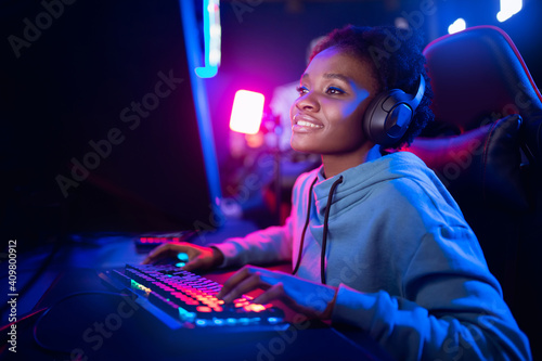 Professional Streamer African young woman cyber gamer studio room with personal computer armchair, keyboard in neon color blur background