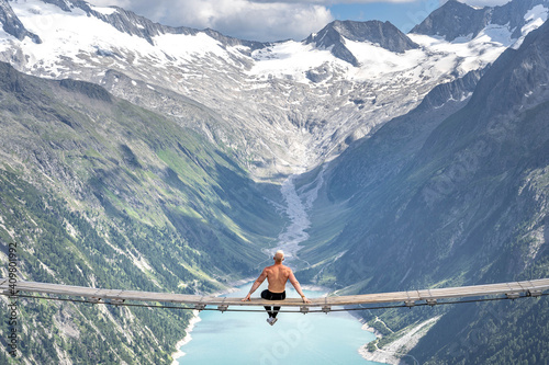 Half naked male sit on swing bridge viewing glacier in Zillertal Alps in summer photo