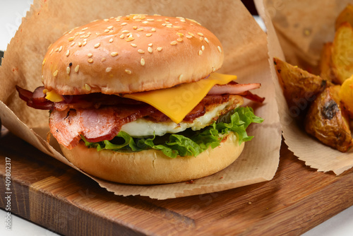 Tasty cheeseburger with fried potatoes rustic style, with sauce, served on a wooden board over white background.