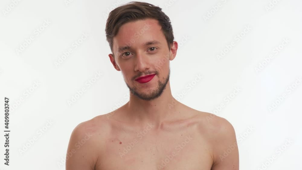 Single thoughtful effeminate half naked young man with brown hair, beard, moustache wear make-up – red lipstick on lips, stare with tenderness directly at camera isolated on white background close-up. Single thoughtful effeminate half naked young man with brown hair, beard, moustache wear make-up – red lipstick on lips, stare with tenderness directly at camera isolated on white background close-up.