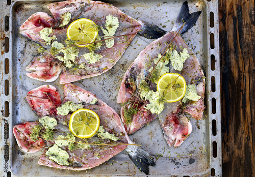 fresco mar dourado peixe com ervas, limão, é sobre um metal cozimento folha, processo de preparação para cozinhar.  photo