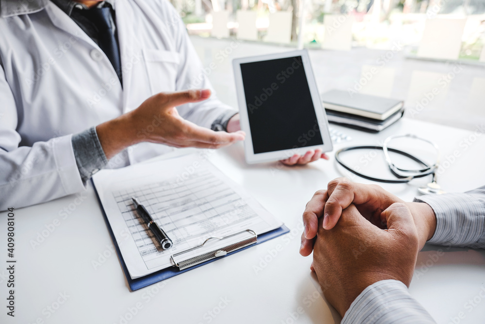 Doctor consulting with patient presenting results on digital tablet tablet sitting at table Doctor consulting with patient presenting results on digital tablet tablet sitting at table