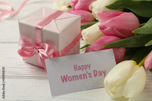 Text Happy Women's Day, tulips and gift box on white wooden background, close up