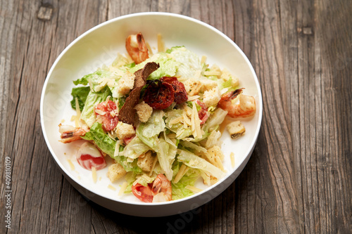 Caesar salad with shrimp on white bowl, on table