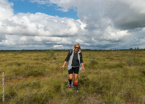 landscape in the swamp, a woman walks through the swamp with swamp shoes and orange rubber boots on her feet