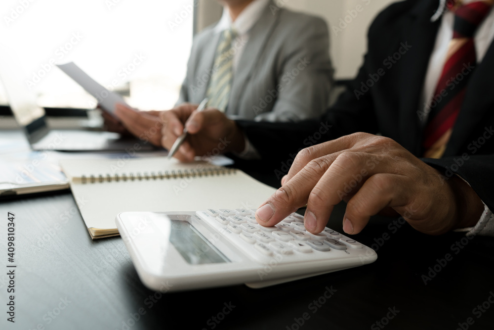 Businessmen use a calculator to calculate company financial statements for their colleagues, view and jointly solve problems within the company. Business finance and accounting concepts Businessmen use a calculator to calculate company financial statements for their colleagues, view and jointly solve problems within the company. Business finance and accounting concepts