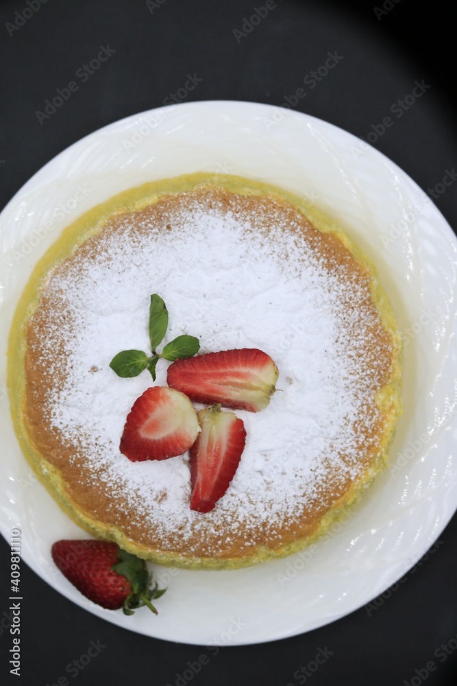 Cheesecake decorated with icing sugar, mint and strawberry in a white plate Cheesecake decorated with icing sugar, mint and strawberry in a white plate