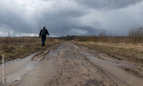 a human figure on a dirty dirt road, old reeds on the side of the road, spring view