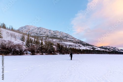Stunning winter view with foot prints in the snow walking away with person standing in distance. Mountains, wilderness, blue sky and pink pastel clouds in background. 