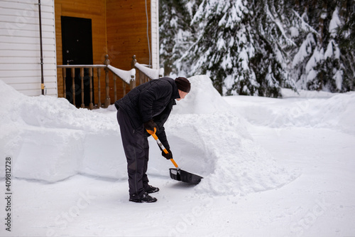 Man scooping snow with a big shovel near house house in countryside after snow storm