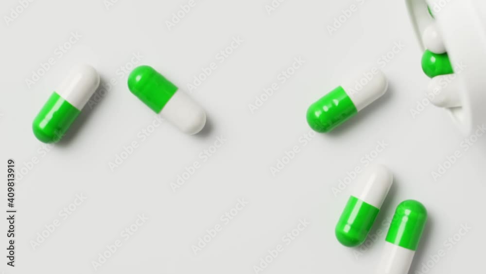 White-green capsules fall out of the bottle onto the table, top view, slow motion. Antiviral drugs, virus protection, Covid-19 treatment. White-green capsules fall out of the bottle onto the table, top view, slow motion. Antiviral drugs, virus protection, Covid-19 treatment.